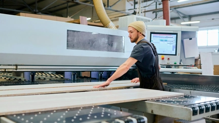 Factory worker operating an automated wood processing machine in a modern manufacturing facility.